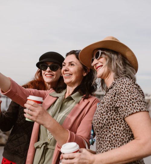 Three women enjoying coffee and taking a selfie together seaside.